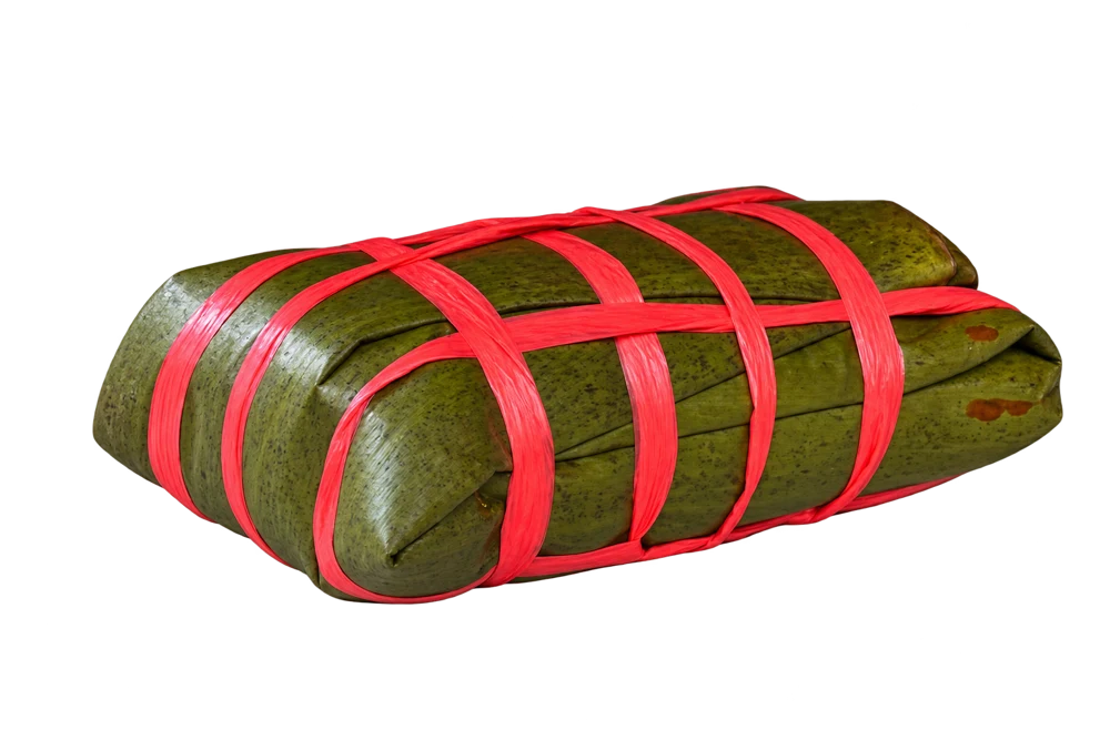 Tamal envuelto en hoja y atado con cinta roja